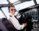 Uśmiechnięty pilot w okularach przeciwsłonecznych i słuchawkach siedzi w kokpicie. Zastanawiasz się, ile zarabia pilot samolotu?