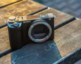 Czarny aparat Sony Alpha ZV-E10 bez obiektywu leży na drewnianym stole, oświetlony ciepłym światłem zachodzącego słońca.