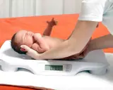 Neonato su bilancia, monitoraggio del calo fisiologico. Le mani sorreggono il piccolo durante la pesata.