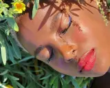 Un volto immerso tra fiori, con un trucco festival audace: eyeliner blu elettrico e labbra rosse vibranti.
