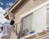 Un hombre pinta las contraventanas de una casa. El trabajo de pintar casas por fuera es esencial para su mantenimiento.