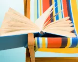 Un libro aperto, pieno di classici della letteratura, appoggiato su una sdraio a righe colorate.