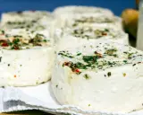 Kilka okrągłych serów labneh z ziołami i przyprawami na białej serwetce.