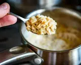 Łyżka gotowanych płatków owsianych, które pomagają obniżyć cholesterol. W tle garnek z owsianką.