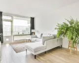 Soggiorno in casa stile nordico con divano grigio, tappeto a righe, piante verdi e grandi finestre.