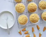 Goldbraune Karottenmuffins auf einem Gitter, daneben eine Schüssel mit Zuckerguss und süße Marzipankarotten. Perfekt für ein Karottenmuffins Rezept!