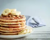 Una pila de tortitas de plátano cubiertas de miel y nueces, con rodajas de plátano fresco encima.