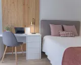 Nowoczesna sypialnia z biurkiem i łóżkiem. Drewniane lamele w sypialni inspiracje tworzą ciepłą atmosferę.