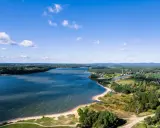 Malownicze jezioro Chańcza otoczone lasami, z piaszczystą plażą i zabudowaniami w tle.