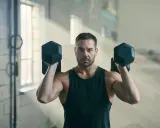 Mann hebt Hanteln im Fitnessstudio. Geduld ist der Schlüssel, wenn man fragt: Muskelaufbau wann sichtbar?