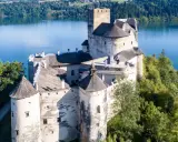 Zamek Dunajec, majestatyczna twierdza na skale, otoczona zielenią i błękitną wodą jeziora.