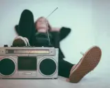 Osoba relaksuje się przy radiomagnetofonie, słuchając muzyki. To pokazuje, jak łatwo dotrzeć do odbiorców, co jest jedną z **zalet reklamy radiowej**.
