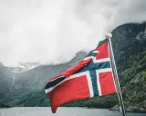 Norweska flaga na tle fiordu. Marzenia o wysokich zarobkach w Norwegii stają się rzeczywistością.