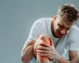 Mężczyzna z grymasem bólu na twarzy trzyma się za kolano, odczuwając silny ból nóg od kolan w dół.