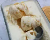 Pyszne lody ciasteczkowe w szklanym naczyniu, z widocznymi kawałkami ciastek i gałkami lodów. Obok leży okrągłe ciastko.