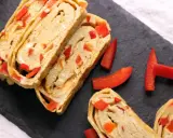 Roladki omletu tamago z kawałkami czerwonej papryki, ułożone na czarnej desce.