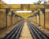 Trabajadores instalan tuberías en una zanja profunda, con estructuras metálicas amarillas para entibar zanjas y prevenir derrumbes.