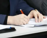 Ręka pisze długopisem po papierze, przygotowując przykładowy artykuł po angielsku na maturę.