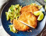 Knuspriges Kohlrabi-Schnitzel mit Gurkensalat und Limettenspalten auf blauem Teller.