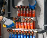Ręce w rękawiczkach dokręcają kluczem elementy instalacji. Trwa podłączenie rozdzielacza podłogówki, zapewniając ciepło w domu.