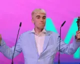 Mc Mata z dwoma statuetkami na scenie, w jasnoniebieskiej marynarce i białej koszuli.