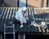 Travailleur en combinaison intégrale sur un toit en fibrociment, préparant le terrain pour une nouvelle peinture. Quelle peinture pour recouvrir peinture au plomb ?