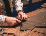 Skräddare arbetar med att laga jacka i tweed. Måttband och tyg på träbord.