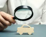 Dłoń z lupą bada drewniany samochodzik. Jak sprawdzić do kiedy OC? To pytanie, na które warto znać odpowiedź.