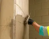 Mano con guante aplica revoque a muros de carga antiguos. Se ve el detalle de la textura y el ladrillo de fondo.
