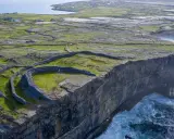 Steile Klippen und alte Steinmauern auf einer grünen Insel vor Galway, Irland. Wellen schlagen gegen die Felsen.