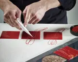 Mains travaillant avec du chocolat plastique rouge pour décorer des carrés de glaçage.