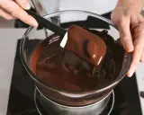 Un chocolat qui ne fond pas ? Ce n'est pas le cas ici ! Une spatule mélange du chocolat fondu brillant dans un bol en verre au-dessus d'un bain-marie.