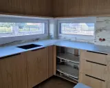 Nowoczesna kuchnia z drewnianymi frontami i marmurowym blatem. Okna sięgają blatu, tworząc wrażenie, co zamiast parapetu.
