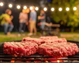 Frische Burger-Patties liegen auf dem Grill. Im Hintergrund feiern Freunde unter Lichterketten. So macht man Hackfleisch selber für den perfekten Grillabend.