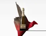 Eine Flasche Piper Heidsieck Cuvée Sublime, umhüllt von fließenden roten und braunen Stoffen, auf einer Glasplatte.