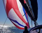 Voile colorée gonflée par le vent, un tableau longueur sandows sur fond de mer scintillante et ciel bleu.
