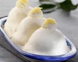 Tre deliziose delizie al limone, guarnite con panna e scorza di limone, in un piatto blu e bianco.