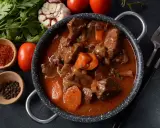 Gęsty, aromatyczny gulasz z sarny w sosie z warzywami. Obok miseczki z papryką i pieprzem, czosnek, pomidory i natka pietruszki.