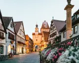 A charming street in gay Germany, with historic buildings, cobblestones, and flowers. Two people on bikes pause to take in the view.
