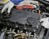 Mechanik w białych rękawiczkach sprawdza stan odmy silnika, demontując pokrywę zaworów.