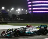 Silberner F1-Rennwagen mit Petronas-Sponsoren fährt bei Nacht auf der Rennstrecke in Bahrain. Flutlicht und ein beleuchtetes Gebäude im Hintergrund.