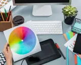 Kolorowe koło barw, tablet graficzny i smartfon na biurku pokazują, czym zajmuje się grafik komputerowy.