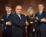 Cztery osoby w garniturach stojące z rękami skrzyżowanymi na piersiach.