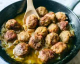 Polpette in bianco cremose in padella, dorate e succulente, adagiate su un letto di cipolle caramellate.