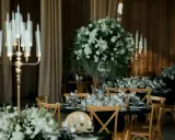 Eleganckie wesele w czarnym stylu. Stoły nakryte czarnymi obrusami, ozdobione białymi kwiatami i złotymi świecznikami.