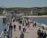 Tłum ludzi spaceruje po molo w Sopocie, jednym z najpopularniejszych gdańsk atrakcje. W tle widać plażę i zabytkowe budynki.