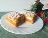 Pyszna szarlotka z bezą i kruszonką, z jabłkami i cukrem pudrem, na białym talerzu, obok kwiatów.