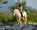 Giovane donna con cappello da cowboy e cavallo bianco durante una passeggiata a cavallo in Campania, tra rocce e vegetazione rigogliosa.