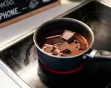 Des morceaux de chocolat noir fondent doucement dans une casserole sur une plaque chauffante, prêts à être transformés en une délicieuse ganache.