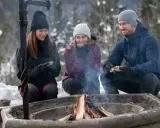 Vänner njuter av värmen från en eld och fika under härliga ute aktiviteter i snöig skogsmiljö.
